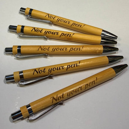 Five wooden pens engraved with the phrase 'Not your pen!' in black script, arranged diagonally on a plain white surface.