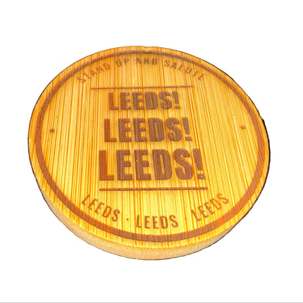 A round wooden coaster featuring the text 'LEEDS! LEEDS! LEEDS!' in dark brown lettering, with 'STAND OF THE SALTIS' and 'LEEDS - LEEDS - LEEDS' engraved around the rim, shown on a dark textured background.