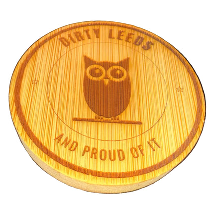 A round wooden plaque or coaster featuring a laser-engraved design of an owl in the center with the text 'DIRTY LEEDS AND PROUD OF IT' on a dark, textured background.