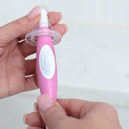 Hand holding a pink children's toothbrush with a white handle against a light background