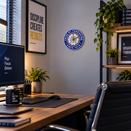 A circular blue and white 'Motto of York' emblem mounted on a gray wall in a modern home office setting with a desk, computer monitor, and plants.