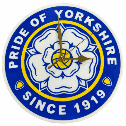 A round wall clock featuring the blue, white, and yellow 'Pride of Yorkshire' rose emblem with gold-toned hands, shown against a plain white background.