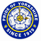 A round wall clock featuring the blue, white, and yellow crest of Pride of Yorkshire, with white hands and no traditional hour markers.