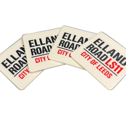 Four white square coasters with rounded corners fanned out on a dark surface. Each coaster features the text 'ELLAND ROAD' in black, with 'CITY OF LEEDS' in red on some coasters and 'LS11' on others.