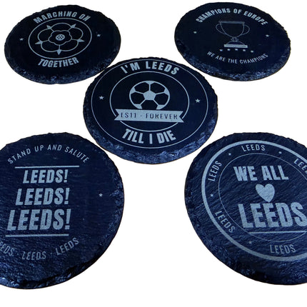 Five round black slate coasters with white printed football-themed designs and text, arranged on a light wood surface.