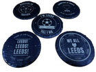 Five round black slate coasters with white printed football-themed designs and text, arranged on a light wood surface.