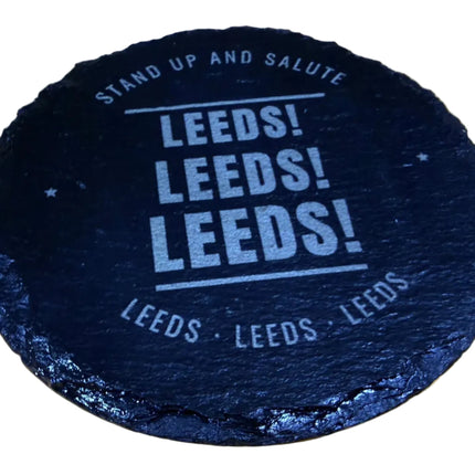 A round black slate coaster with 'LEEDS! LEEDS! LEEDS!' printed in white, resting on a light wood background.