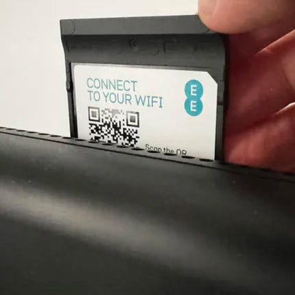 A close-up of a hand holding a small black card labeled 'CONNECT TO YOUR WIFI' with a QR code and blue circular 'E' icons, positioned above a black surface.