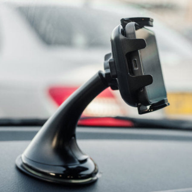 A black suction cup car phone mount holding a smartphone, attached to a dashboard with a blurred car window in the background.