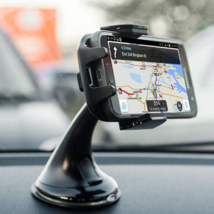 A black car windshield GPS mount holding a tablet-style navigation screen, shown attached to a dashboard inside a vehicle with a blurred outdoor background.