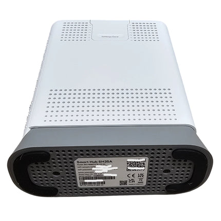 A white and gray smart home network hub device, shown from the back with a perforated metal grille and a product label sticker.